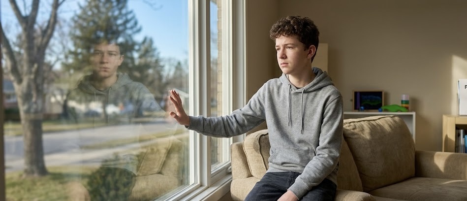 Anxious teen boy looks out window